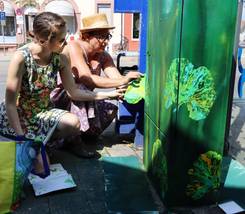 Bei der Arbeit von Larissa Fabich (vorne) und Hannah Sirrett werden Blätter und andere Pflanzenteile mit Acrylfarbe bestri-chen. Diese dienen dann als „Stempel“, um die Motive auf dem Verteilerkasten zu erzeugen. ©Foto: Schaible/Stadt Langen